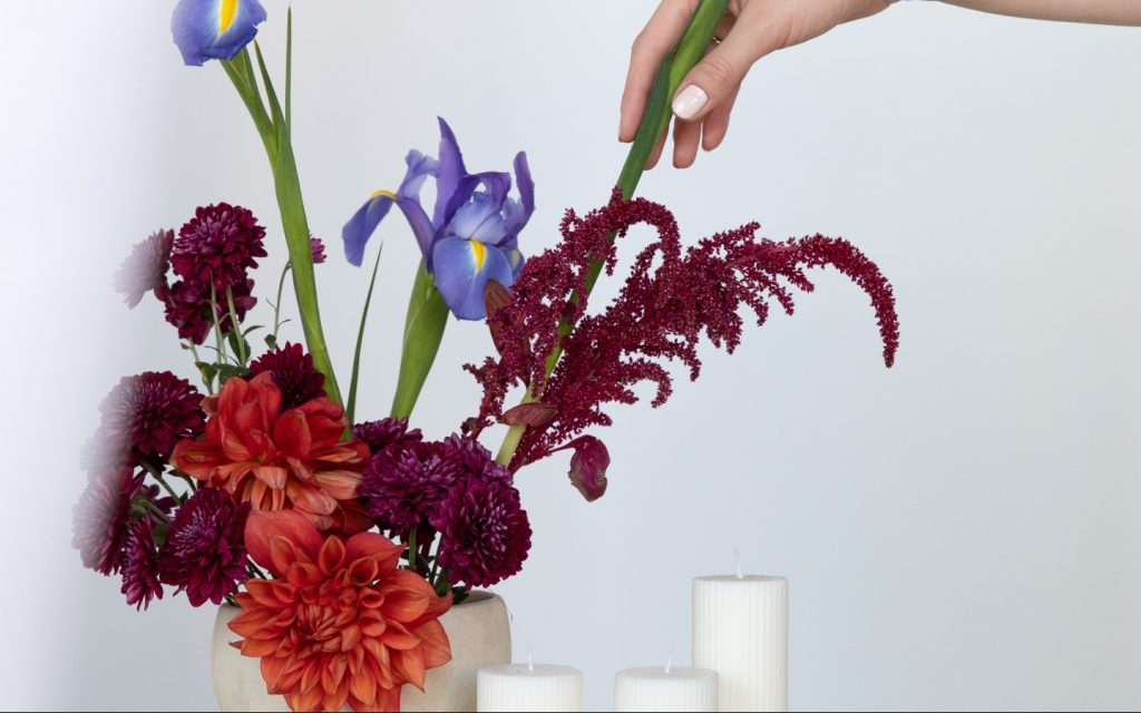 Stylist arranging a floral centrepiece with irises and amaranthus, wedding styling