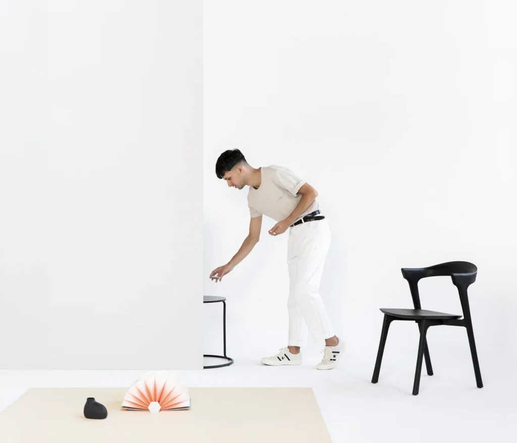 Stylist arranging a vase on a stool beside a black chair in a white studio