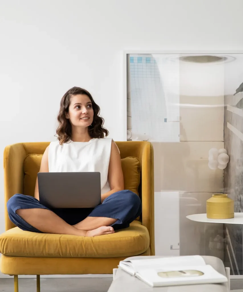 Diploma of Interior Design student working on a laptop in a mustard armchair